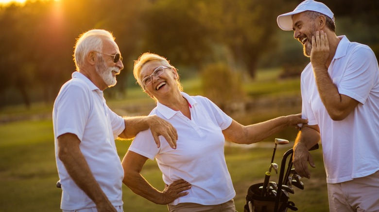Three seniors wearing white talking and laughing on a golf course
