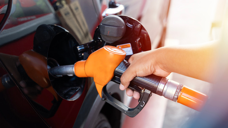 A hand on a gas pump, fueling a car in the sunshine.