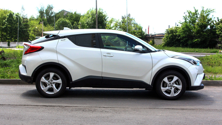 White New SUV Toyota C-HR Hybrid Crossover the city street on the background of green trees.
