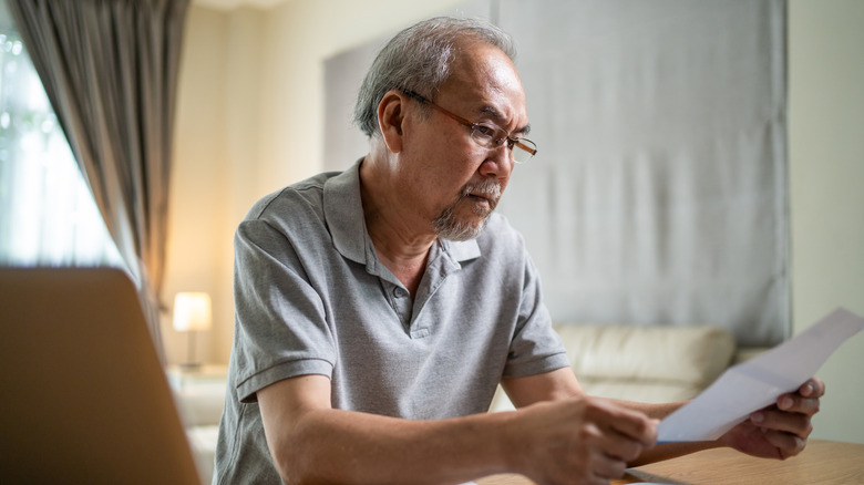 Stressed older Asian man looking at a bill