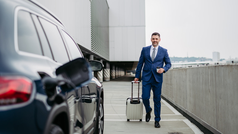 Business man approaching car with luggage and coffee cup