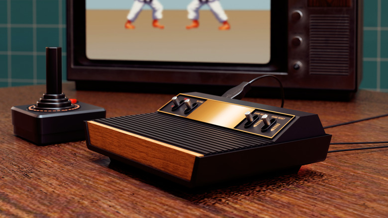 An Atari 2600 and a joystick in front of a screen displaying a fighting game