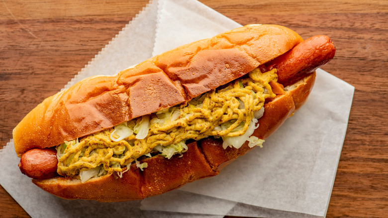 A pork sausage in a hot dog bun topped with classic condiments mustard, ketchup and sauerkraut.