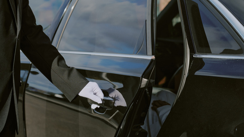 A gloved hand opens a black luxury car.