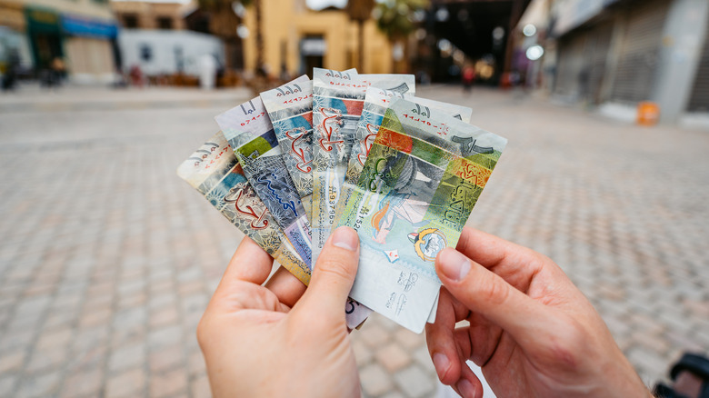 Young man holding Kuwaiti dinar on the street in Kuwait City in Kuwait