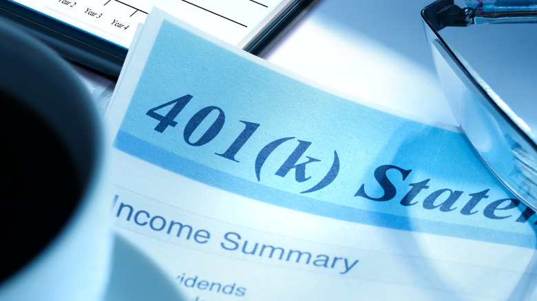 A cup of coffee rests on a desktop next to a 401k account statement with a smart phone in the background.
