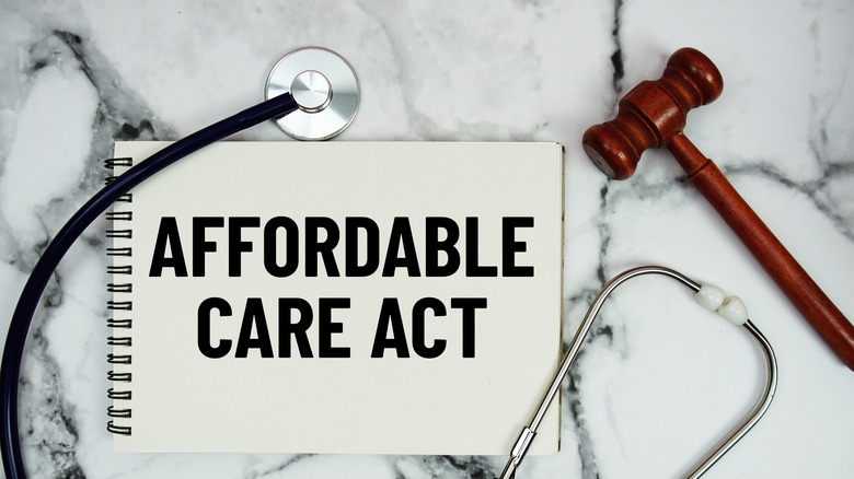 Affordable Care Act text written on notepad with stethoscope and gavel on marble background.
