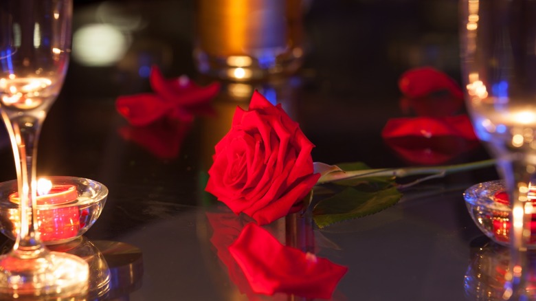 A red rose on a table with a candle and champagne flutes similar to props used on The Bachelor show.
