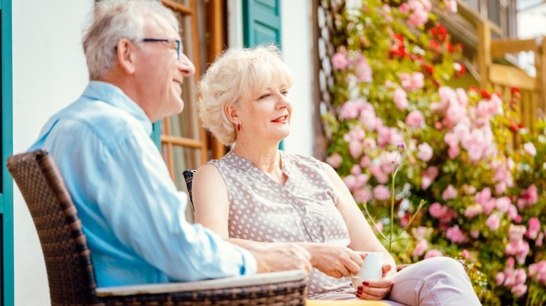 An elderly retired couple sitting outside on their porch having tea.