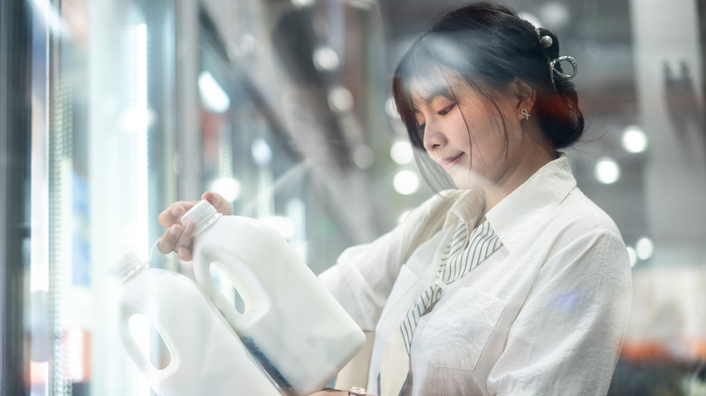 A woman holding and reading the label on two jugs of milk at the grocery store.
