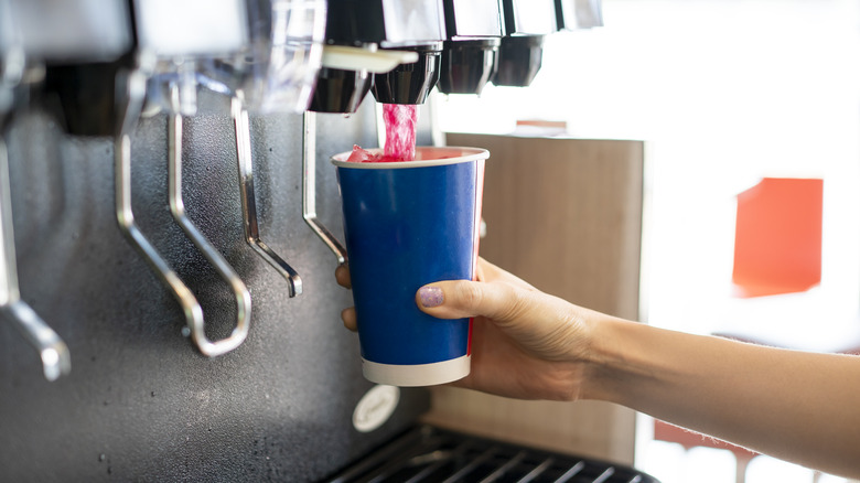 The hand of a person fetching a fizzy drink from a machine