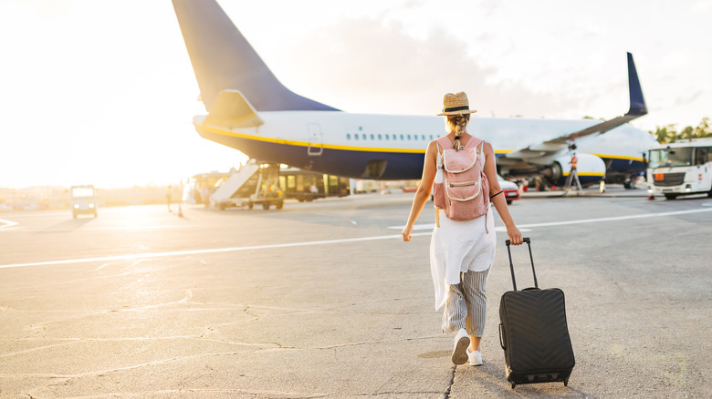Traveler approaching plane on tarmac carrying suitcase