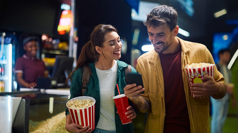 Couple carries movie snacks while checking phone