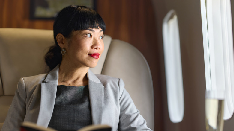 A wealthy middle aged woman reading a book and looking out a window