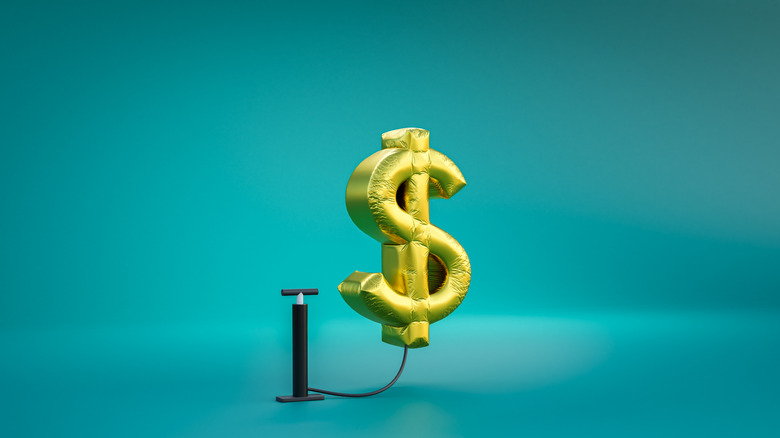 Gold balloon in shape of dollar sign connected to air pump.