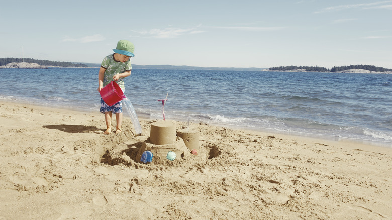 boy filling moat around sand castle with water