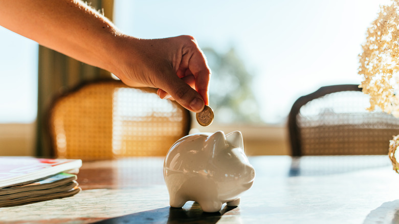 Hand angling to drop a coin in a small white ceramic piggybank