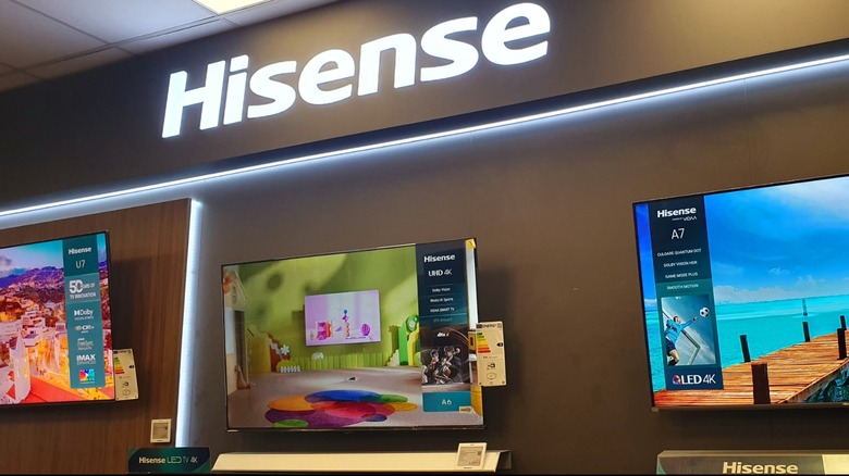 Three Hisense TVs arranged against a wall with a glowing Hisense logo above the wall