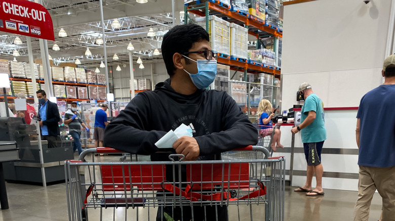 A man wearing a mask holding his shopping cart with grocery in the Costco check out area