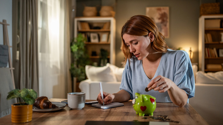 woman putting money in piggy bank and writing notes in planner