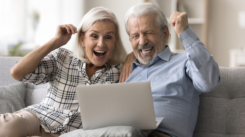 Happy elderly spouses clenching their fists making winners gesture sitting on sofa