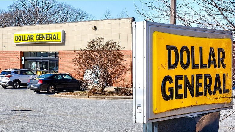 Dollar General sign in the foreground and two cars parked outside a Dollar General in the background
