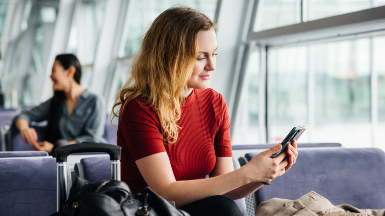A young woman checking her cellphone in an airport seating area