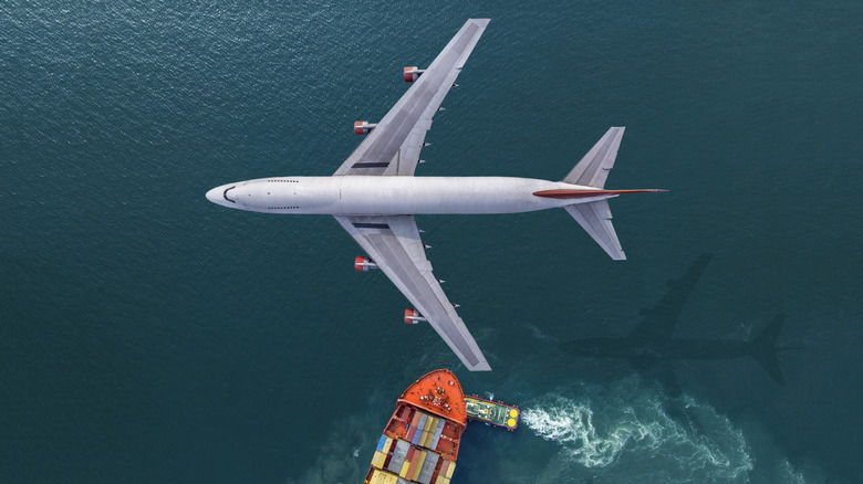 A passenger plane flies over the sea, being crossed at a perpendicular angle by a cargo ship, in this image that represents international shipping.