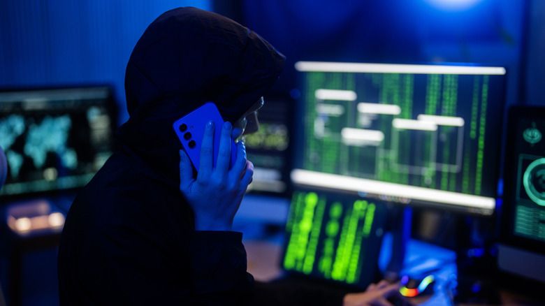 Obscured masked face using laptop computer for cyber attack and calling on cellphone