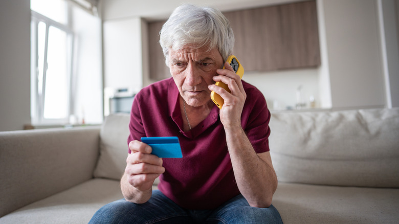 An older man on the phone while looking at his credit card.
