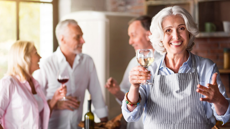 A happy elderly woman smiling in the kitchen while having a drink and enjoying celebration with her family