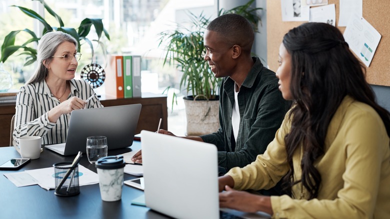 A young couple sitting in an office with a mature woman seated behind a laptop.