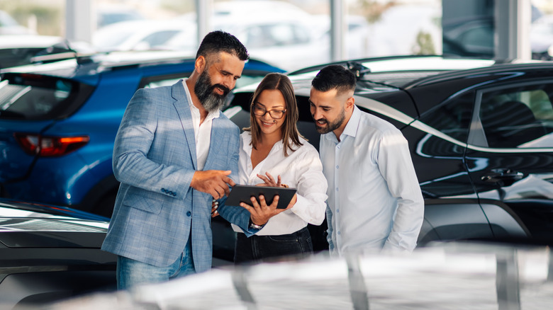 A car salesperson shows a young couple some data on a tablet in a dealership