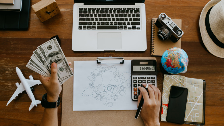 Person budgeting for a trip with cash and a calculator in hand