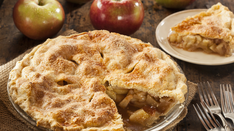 Apple pie sitting next to fresh applies and forks