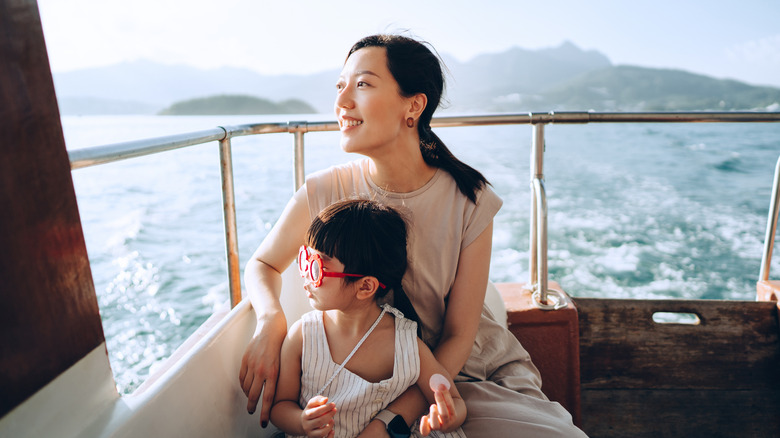 A woman seated on a ship deck with her young daughter staring out into the ocean.