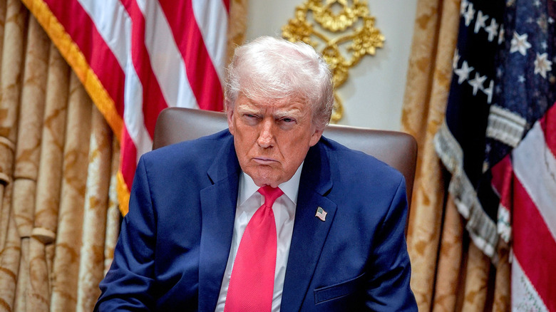 President Donald Trump sitting in a chair with U.S. flags behind him