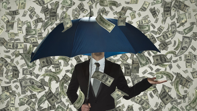 A person holding up an umbrella while a rain of dollar bills fall on him