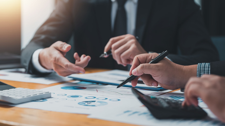 hands pointing to paper, pen, and calculator