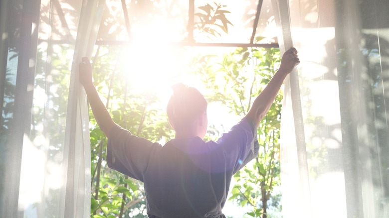 Woman opening curtains to morning sunshine
