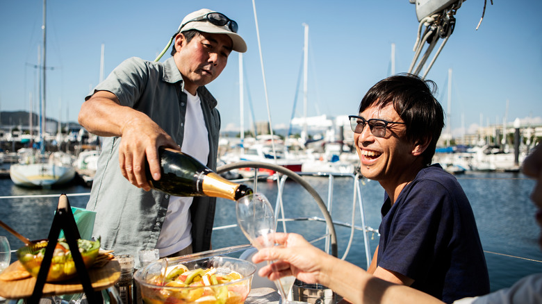 A man pouring champagne next to a smiling man on a private yacht.