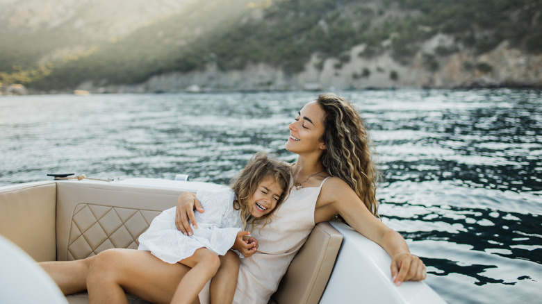 A little girl laughing in he rmother's lap in a boat floating on sparkling water.