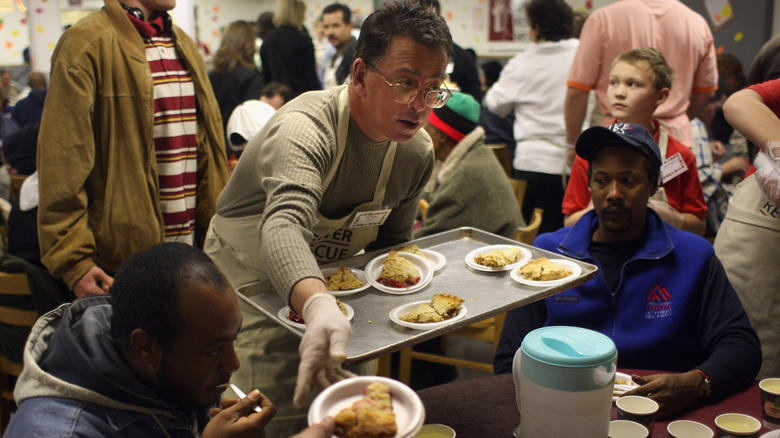 Man hands out small plates of food to seated individuals