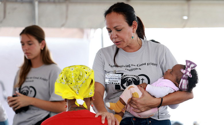 Woman holding infant touches sitting mother while a younger woman stands in background