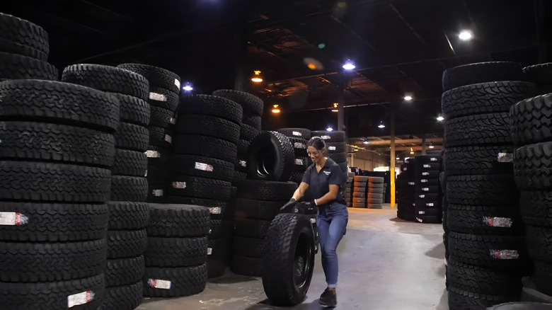 A TreadWright staff rolling a tire between two stacks of arranged tires in a TreadWright warehouse