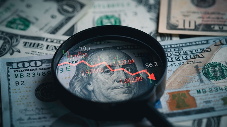 magnifying glass on $100 bill with downward arrow