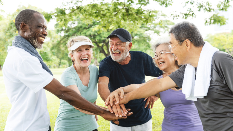 diverse group of older adults laughing and holding hands in a circle