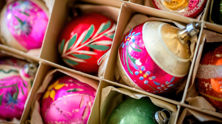 A collection of round glass Christmas ornaments in different colors and designs separated in a box by cardboard partitions.