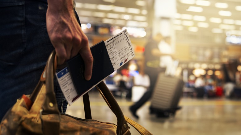 A man's hand holding a passport and bag