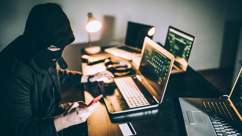 A cyber criminal using a phone and several laptops